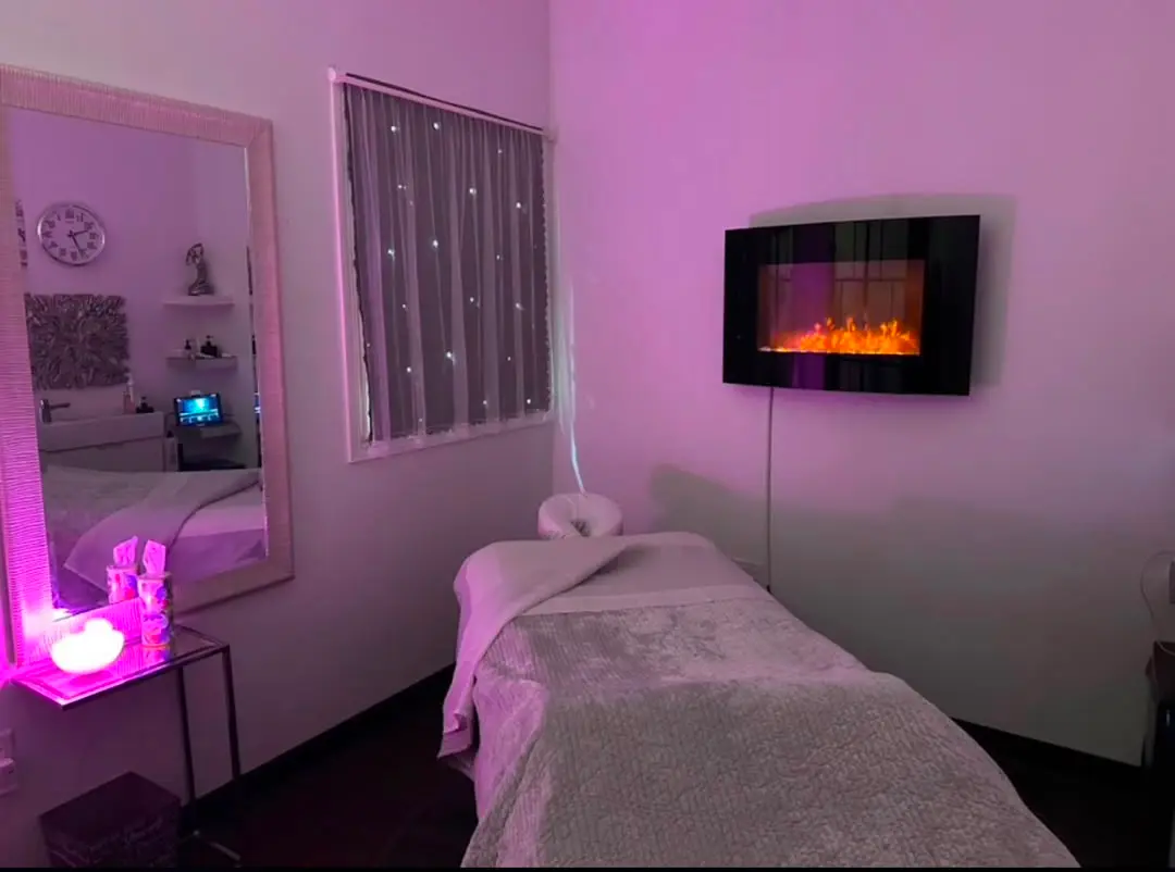 The Bliss Haven treatment room: a draped massage table in soft, warm light beside a wall fireplace